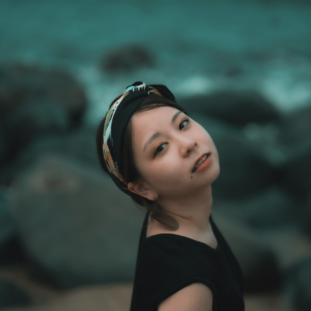 福岡県糸島市二見ヶ浦の海辺で撮影したポートレートモデルSerinaさんの写真　大きな岩がいくつもころがる浜辺を背にこちらを見つめています