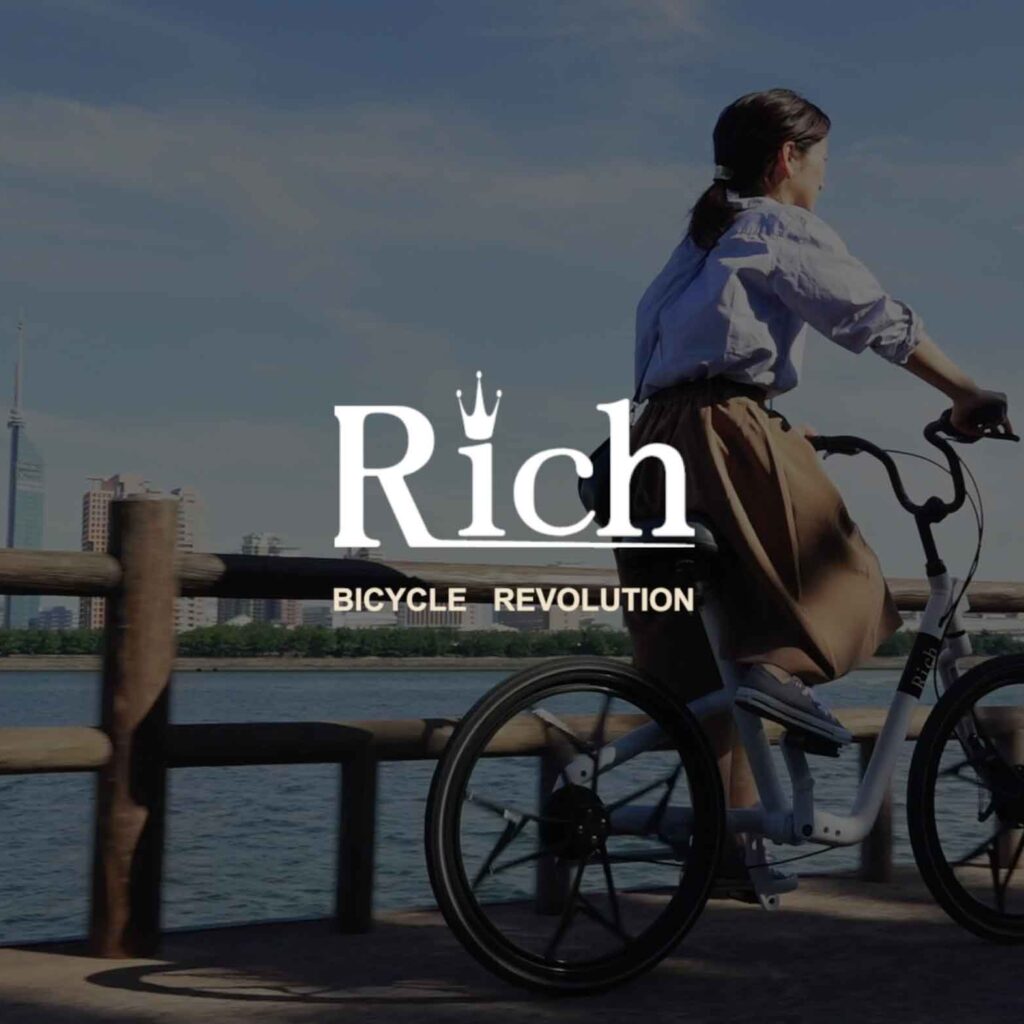 メンテナンスフリー自転車Richのプロモーションビデオサムネイル　海沿いの道を自転車で走る女性の写真