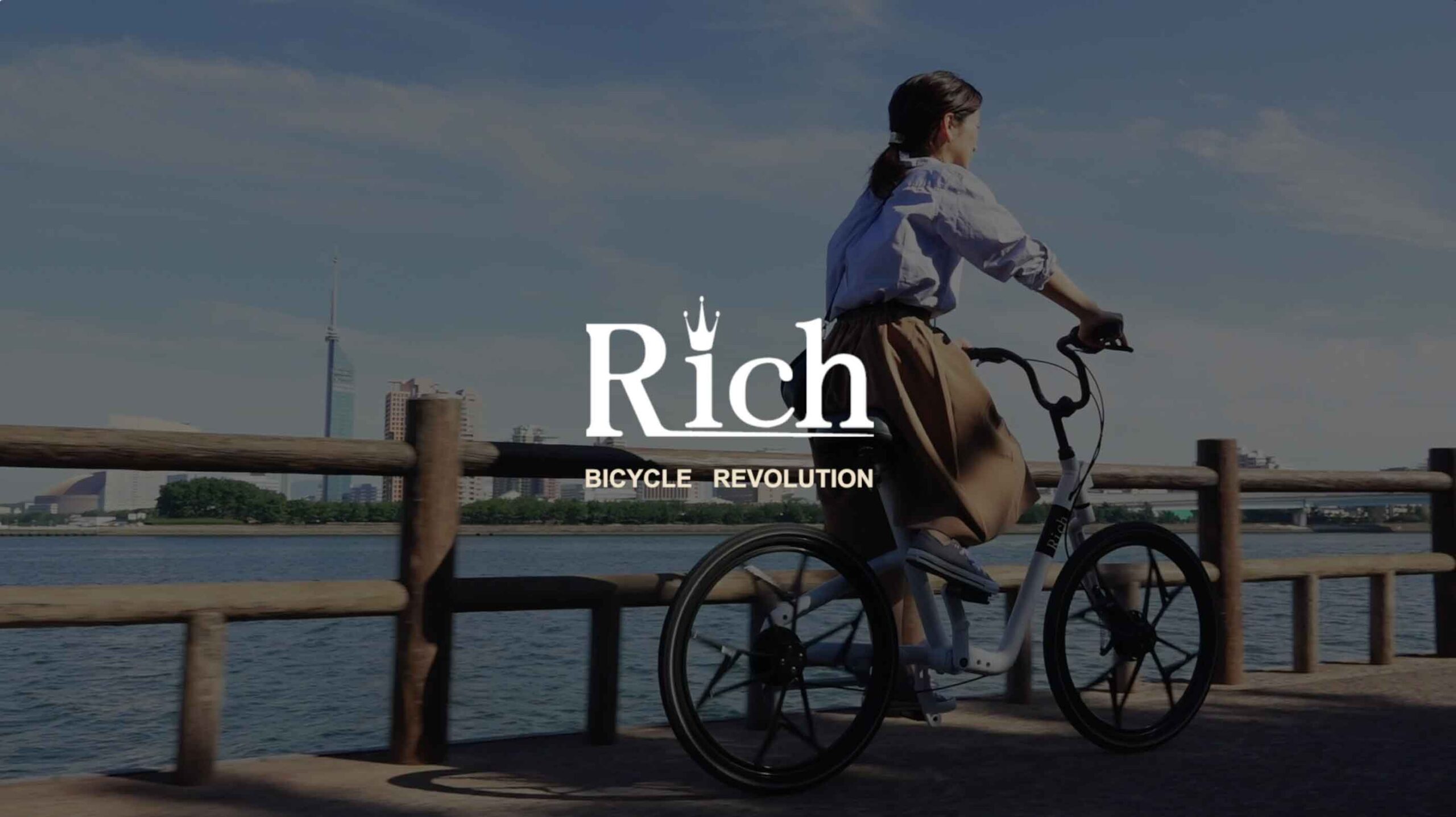 メンテナンスフリー自転車Richのプロモーションビデオサムネイル　海沿いの道を自転車で走る女性の写真